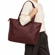 Burgundy sheepskin leather tote worn over shoulder with cream sweater on white background